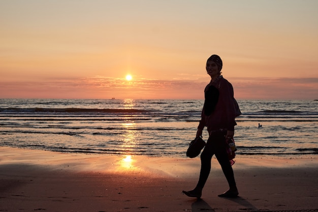 Sylwetka osoby idącej brzegiem morza o zachodzie słońca