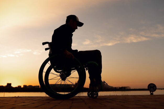 Zdjęcie sylwetka osoby niepełnosprawnej na wózku inwalidzkim na tle wysokiej jakości zdjęcia zachodzącego słońca