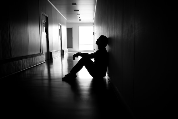 Sylwetka przygnębionego mężczyzny siedzącego na chodniku budynku mieszkalnego Smutna i samotna koncepcja