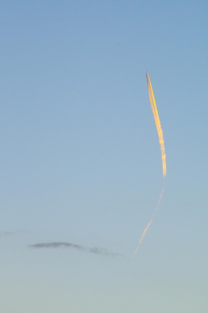 Zdjęcie sylwetka samolotu pasażerskiego ze smugą kondensacyjną w chmurach oświetlona jasnym zachodem słońca