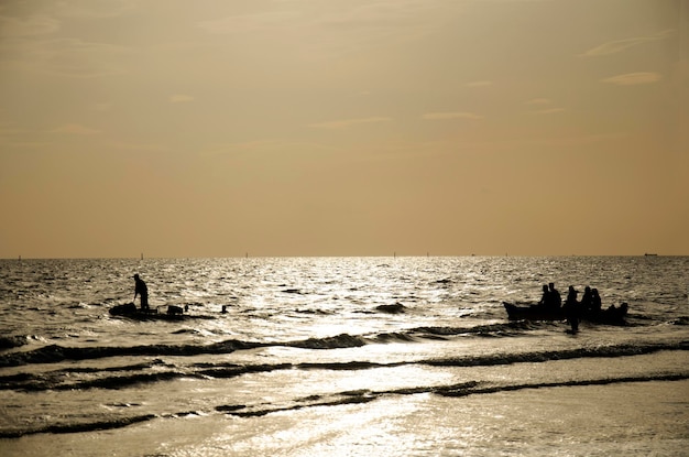 Sylwetka Tajowie i podróżnicy podróżują i bawią się skuterem wodnym i bananową łodzią z falą na morzu na plaży Bangsaen w czasie zmierzchu w Chonburi Tajlandia