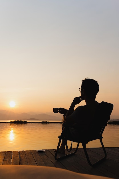 Sylwetka turysta siedzi na krześle trzymając filiżankę kawy oglądając wschód słońca
