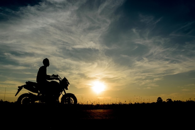 Sylwetka wizerunek młodego człowieka podróż motocyklem przy zmierzchem.