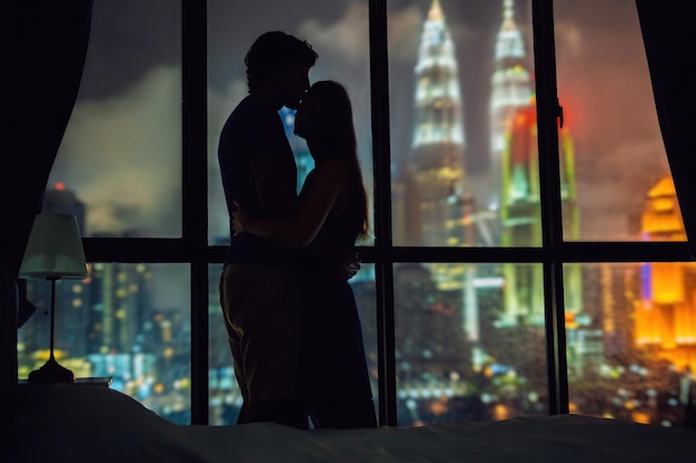 Sylwetka zakochanej pary na tle okna z widokiem na nocne miasto