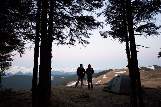 Sylwetki dwóch mężczyzn stojących obok namiotu na szczycie góry podczas wspólnego biwakowania