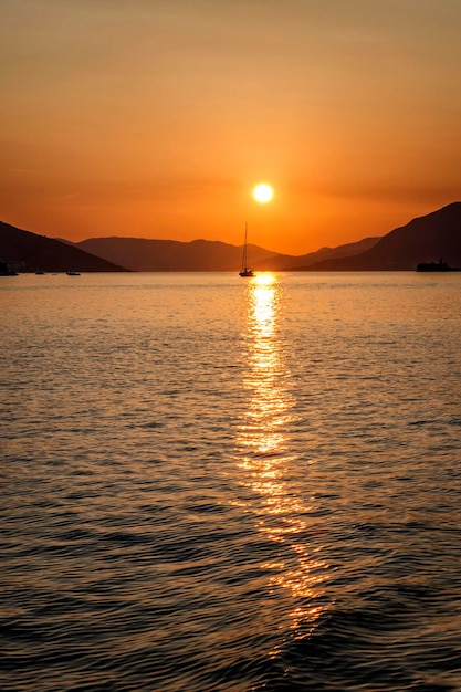 Sylwetki jachtów żaglowych na tle jasnopomarańczowego zachodu słońca na morzu Romans i relaks Wspaniały krajobraz Pionowy