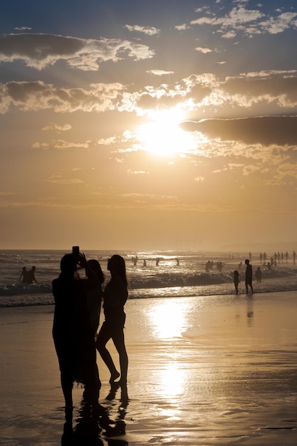 Sylwetki ludzi robiących zdjęcia na plaży o zachodzie słońca