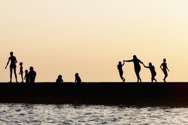 Sylwetki ludzi skaczących z morskiego molo Odpoczynek na morskiej plaży