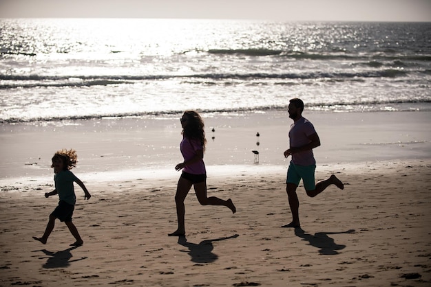 Sylwetki rodziny biegającej wzdłuż morskiej plaży o wschodzie słońca Ćwiczenia na świeżym powietrzu sylwetki biegaczy sport i zdrowy, rodzinny styl życia