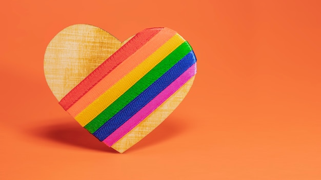 Symbol LGBT. Drewniane serce z tęczą LGBT na pomarańczowym tle.