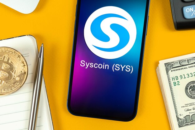 Symbol monety Syscoin. Handluj kryptowalutami, cyfrowymi i wirtualnymi pieniędzmi, bankowością z koncepcją telefonu komórkowego. Biznesowy obszar roboczy, stół ze zdjęciem z widokiem na laptopa