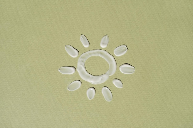 Symbol słońca wykonany z białego kremu rozmazanego na zielonym tle Estetyczna koncepcja produktu kosmetycznego