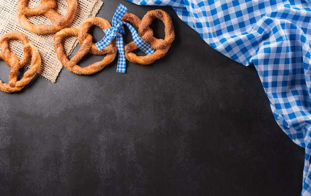 Symbole dekoracji festiwalu Oktoberfest wykonane z bochenka precla i bawarskiej białej i niebieskiej tkaniny na ciemnym kamiennym tle