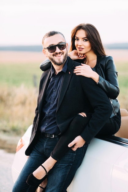Sympatyczna para mąż i żona spędzają czas poza miastem siedząc na masce samochodu