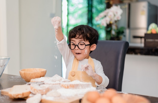 Syn gotuje jedzenie. Przygotowanie składnika z mąki i chleba. Codzienny styl życia dziecka w domu. Azjatycka rodzina w kuchni.