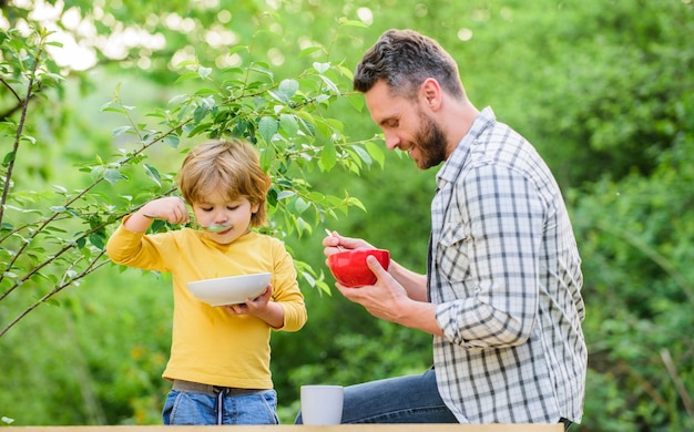 Syn i ojciec jedzą na świeżym powietrzu Szczęśliwa rodzina razem weekend rano śniadanie szczęśliwy dzień ojca Mały chłopiec z tatą jedzą płatki zbożowe zdrowa żywność i dieta Produkty mleczne Wybór żywieniowy