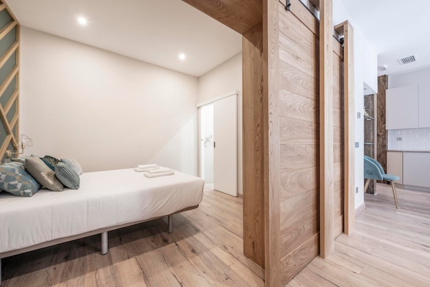 Sypialnia z dużym łóżkiem z białą pościelą zielone poduszki w kolorze ściany przesuwane drewniane drzwi drewniane półki i kasztanowe podłogi