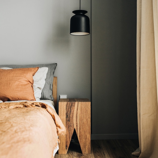 Sypialnia z łóżkiem, ruda narzuta, poduszki, dębowa szafka nocna, designerska lampa wisząca, drewniana podłoga.