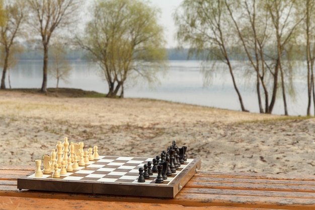 Szachownica z szachy na drewnianej ławce z tłem nabrzeża rzeki. Gra w szachy na świeżym powietrzu z drewnianymi szachami