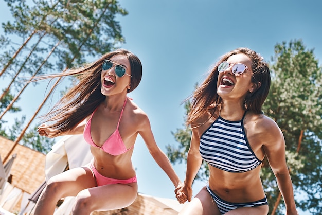 Szaleje, szaleje, dwie atrakcyjne i zabawne młode kobiety w stylowych strojach kąpielowych i okularach przeciwsłonecznych