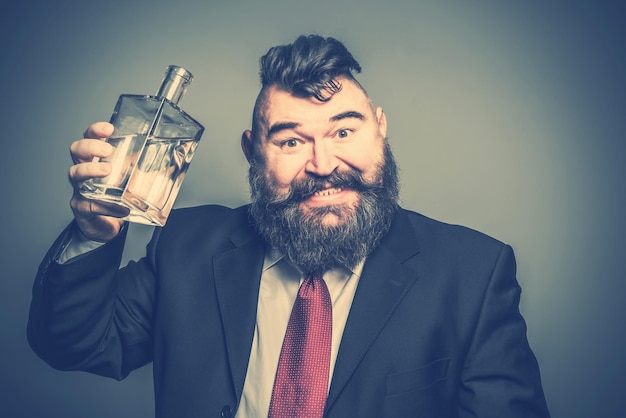 Szalony brodaty mężczyzna w garniturze podnosi butelkę alkoholu Stonowany