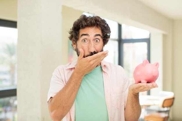 Zdjęcie szalony brodaty mężczyzna zakrywający usta dłonią i zszokowany lub zaskoczony wyrazem koncepcji skarbonki