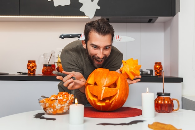 Szalony mężczyzna rzeźbi twarz na dyni przygotowując ją na Halloween