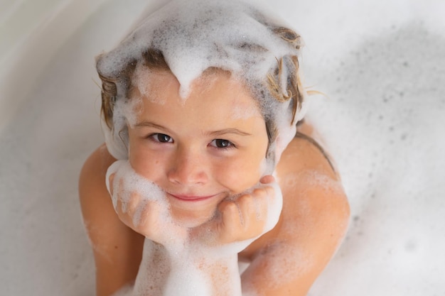 Zdjęcie szampon dla dzieci z pianką szamponową i bąbelkami na włosach podczas kąpieli śmieszna twarz dziecka w piankowych włosach