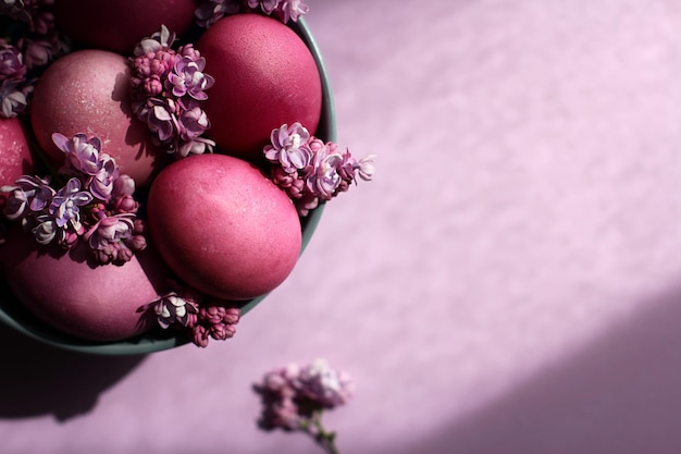 Szara miska z jasnoróżowymi pisanki i kwiatami bzu na fioletowym tle wystrój wielkanocny selec