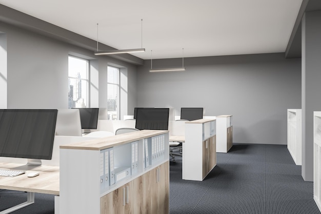 Szara ściana otwarta przestrzeń biurowa z betonową podłogą, dużymi oknami i rzędami biurek komputerowych. Makieta renderowania 3D
