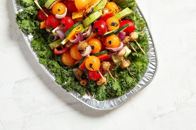 Szaszłyki wegetariańskie z suszonymi ziołami na drewnianych szaszłykach z pomidorów z cukinii i cebuli na talerzu