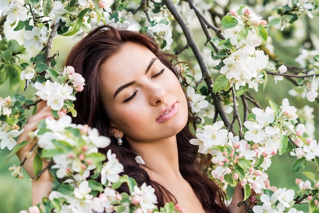 Szczegół portret pięknej kobiety w ogrodzie wiosną. Dziewczyna z zamkniętymi oczami wdycha zapach kwitnących drzew.