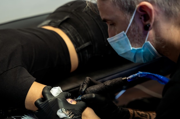 Szczegóły rąk i maszyn tatuażysty pracującego na ramieniu nierozpoznawalnej kobiety