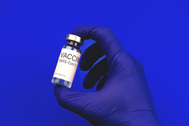 Szczepienie COVID-19, lekarz ręka w niebieskich rękawiczkach trzyma fiolkę ze szczepionką, koncepcję szczepień i samoopieki