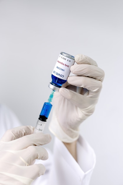 Szczepionka COVID-19 w rękach badacza, nierozpoznawalna lekarka trzyma strzykawkę i butelkę ze szczepionką na koronawirusa.