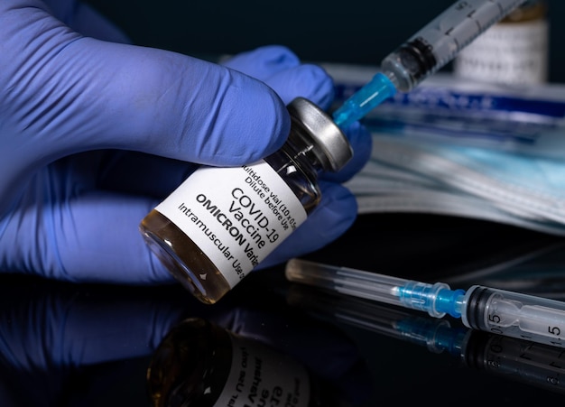 Szczepionka przeciwko koronawirusowi Covid19 opracowana dla wariantu Omicron trzymana w rękawiczce z igłą strzykawki podskórnej i nowymi strzykawkami w tle