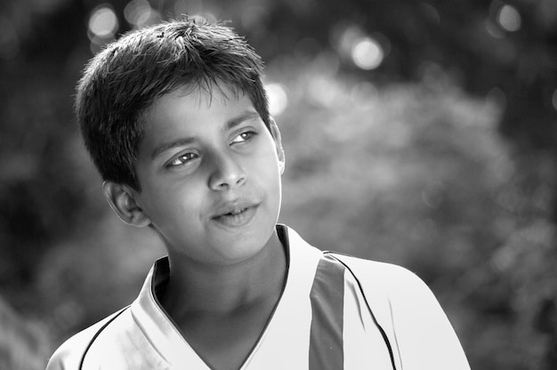 Szczere zdjęcie portretu młodego indyjskiego chłopca z bliska twarz patrząc na odległość w czerni i bieli