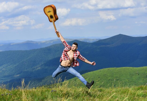 Szczęście hipster moda western camping i wędrówki szczęśliwy i wolny kowboj człowiek z nagim muskularnym torsem gitarzysta akustyczna muzyka country piosenka seksowny mężczyzna z gitarą w kraciastej koszuli