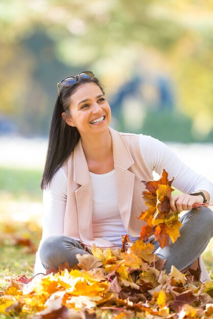 Szczęście kobieta siedzi w parku jesień trzymając bukiet z liści jesienią.