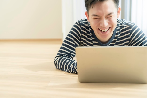 Szczęście spokojny uśmiech azjata ciesz się pracą w domu kwarantanna relaks i pozytywna praca z laptopem azjata atrakcyjny sprytny freelancer korzystaj z laptopa na laminowanej drewnianej podłodze