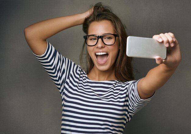 Szczęście to zrobienie idealnego selfie za pierwszym razem Zdjęcie studyjne atrakcyjnej młodej kobiety robiącej selfie na szarym tle