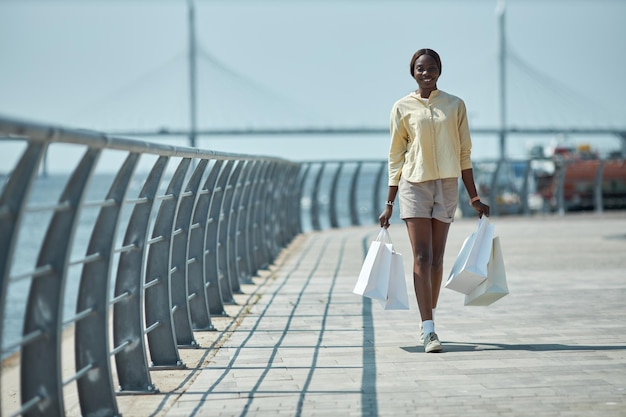 Szczęśliwa Afroamerykanka z torbami na zakupy chodząca po molo na świeżym powietrzu