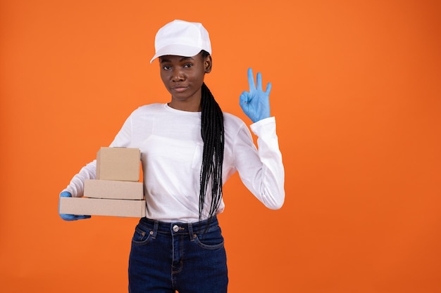 Szczęśliwa afroamerykańska dziewczyna dostarczająca w białej czapce i niebieskich gumowych rękawiczkach przyciśniętych do bocznych pudełek