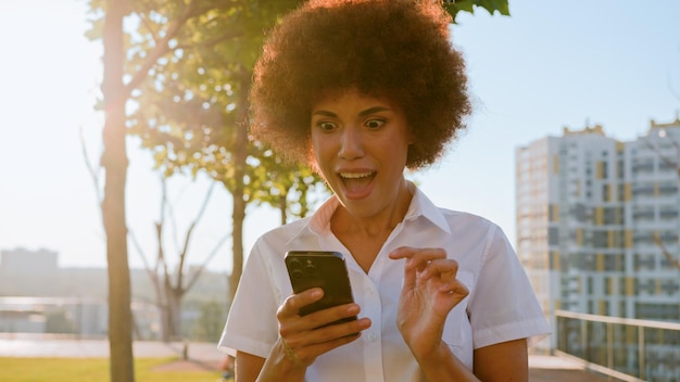 Zdjęcie szczęśliwa afroamerykańska kobieta biznesu cieszy się sukcesem telefon komórkowy zwycięstwo miasto słońce tło radosne
