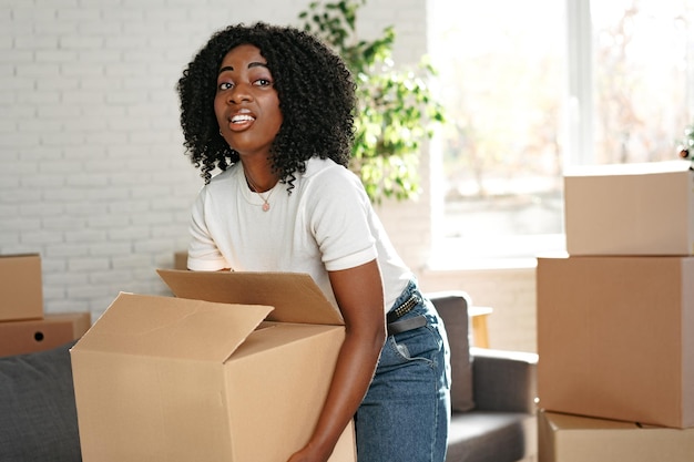 Szczęśliwa afrykańska młoda kobieta z kartonowym pudełkiem przenosi się do nowego miejsca