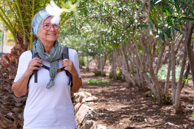 Szczęśliwa aktywna starsza kobieta z plecakiem na wycieczce na świeżym powietrzu, ciesząc się zdrowym stylem życia i słonecznym dniem