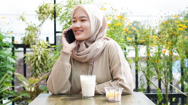 Szczęśliwa Asia hidżab kobieta za pomocą inteligentnego telefonu i dzwoniąc, siedząc w kawiarni