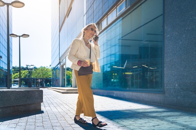 Szczęśliwa atrakcyjna bizneswoman rozmawiająca ze swoim smartfonem przed nowoczesnym budynkiem