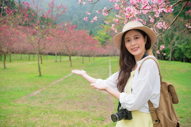 szczęśliwa atrakcyjna podróżniczka wykonująca gest pokazujący w podróży po japonii i prezentująca kwiat wiśni podczas zwiedzania słynnego parku roślin drzew sakura.