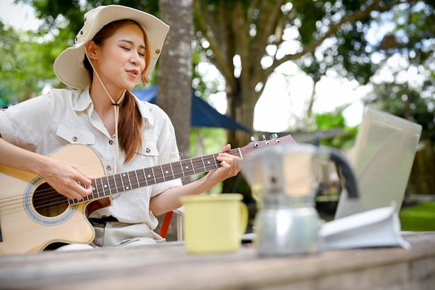 Szczęśliwa Azjatka śpiewa piosenkę podczas gry na gitarze podczas wakacji w naturalnym parku